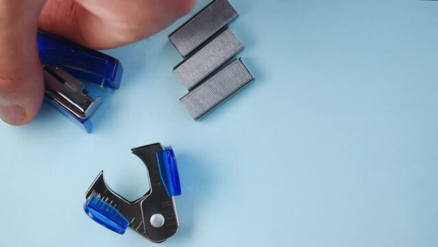 Close-up view of a hand choosing a stapler over staples, and a staple remover on a table