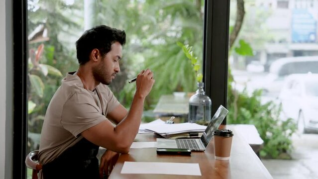 Indian man Is taking a serious thought into auditing accounts. And can't manage cost of a small coffee shop. which he owns, checking accounting documents with a laptop computer family small business