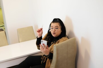 Cheerful young woman using her smartphone to shop online while lounging in her comfortable home