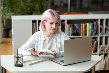 Hipster teen girl student with pink hair watch video online webinar learn on laptop at library