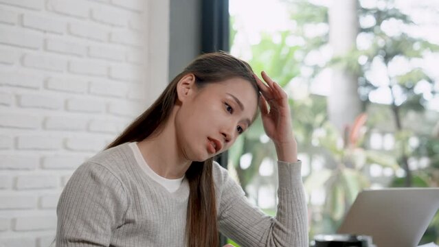 Pretty Asian woman checking account of small business cafe and showing a stern expression from the problem of spending more than income Make sure it matches the laptop computer page file.