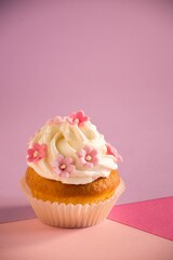 Appetizing cupcake with a pink frosting and decorative sprinkles on a pink surface