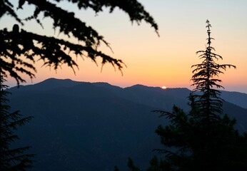 Scenic view of sun setting behind a green mountain range