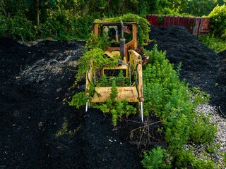 Old and rusted tractor, overgrown with green vines and black mulch on Long Island, New York