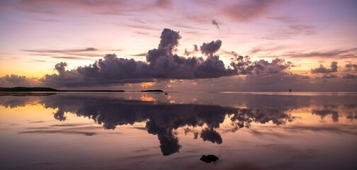 Tranquil pink sunset with large fluffy clouds over the sea reflecting on the water
