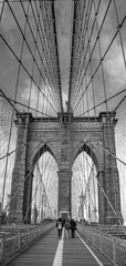 Vertical grayscale shot of people walking on Brooklyn Bridge in NYC, USA - obrazy, fototapety, plakaty