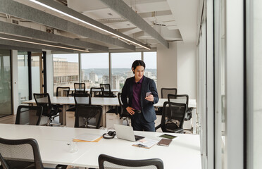 Fototapeta premium Handsome asian man holding mobile phone, using smartphone, standing in modern office, meeting room