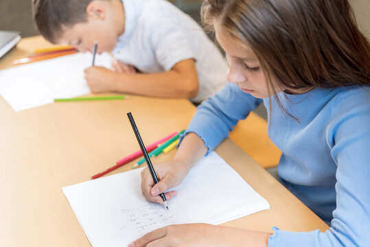 Two primary school pupils at their desks in class, close up. A schoolgirl and a schoolboy leaned over notebooks and write mathematical tasks. The importance of developing correct posture at the desk