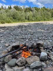 small camp fire in riverbed with forest and blue sky