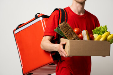 Delivery Concept. Handsome delivery man in a red uniform carrying paper box of grocery food and drink from store isolated on white studio background. Copy Space.