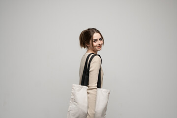 Happy, smiling brunette young woman carrying reusable cotton bag. Concept of recycle for better environment. No plastic.