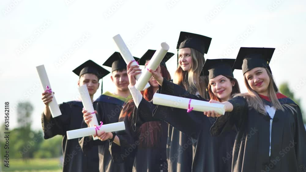 Wall mural Cheerful graduates waving their diplomas on a sunny day.