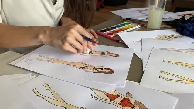 A woman draws sketches of swimwear and underwear with a pencil.