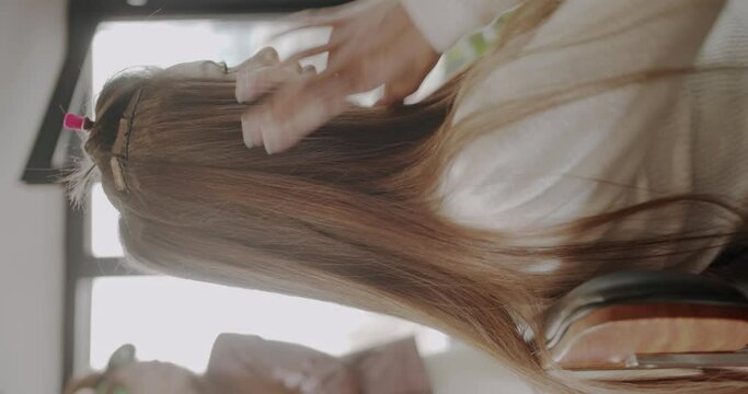 Adding hair extensions in the same color as original hair, professional hairstyling salon, vertical video