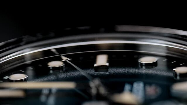 Extreme closeup of yellow second arrow passing by on blue clock face. Lengthwise view of luxury swiss watch. Closeup real time shot. Running second arrow