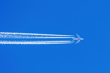 Huge Airplane at cruising altitude with long white contrail in blue sky
