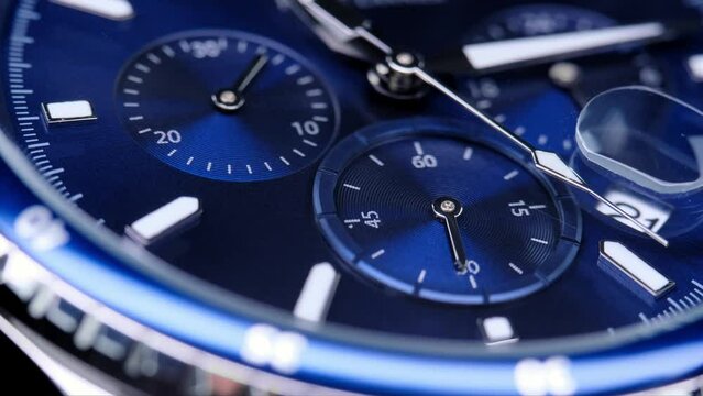 second hand ticking on a blue watch face. Men's chronograph watch in metal with sapphire crystal. closeup view of rotating watch, running second arrow. blue dial