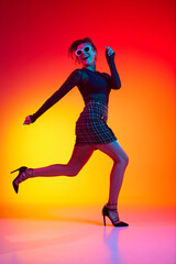Fototapeta na wymiar Full lenght photo of running woman wearing fashionable with sunglasses in transparent top and skirt posing over gradient yellow-red neon background.