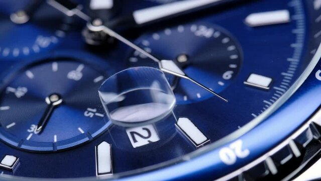 second hand ticking on a blue watch face. Men's chronograph watch in metal with sapphire crystal. closeup view of rotating watch, running second arrow. blue dial