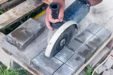 A worker on the street cuts paving slabs with a grinder for further paving on a sunny summer day