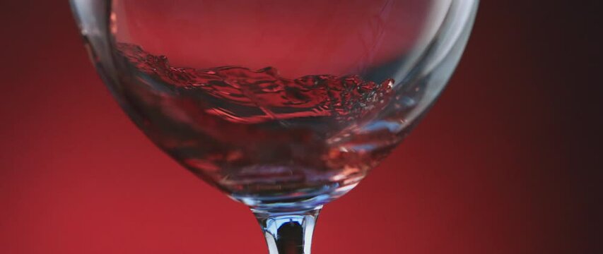 Close-up shot of red wine pouring from bottle into goblet over red background. Rose wine pour into glass