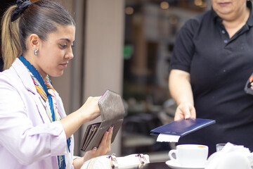 Waitress brings the bill to pay the girl in cafe. Young woman holds her wallet.