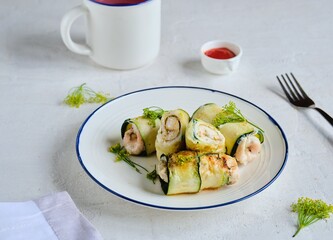 Fried chicken rolls wrapped with sliced zucchini on a white plate on a light concrete background. Recipes for zucchini.