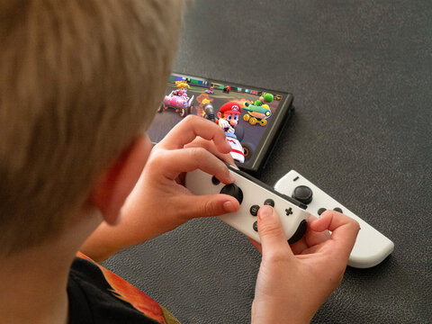 Young boy playing Mario Kart on a popular new Nintendo Switch console in handheld mode. Close up image on hands. Copenhagen, Denmark - August 5, 2023.
