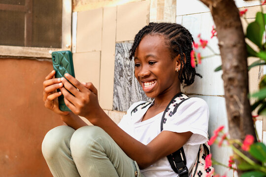 A young African girl sitting on the ground looking at her cell phone