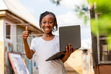 A young girl holding a laptop and giving a thumbs up