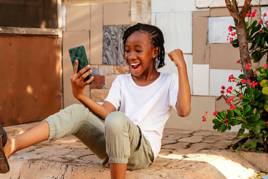 A young African girl sitting on the ground looking at her cell phone