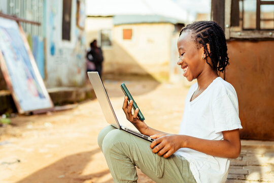 young African girl using technology while sitting on the ground