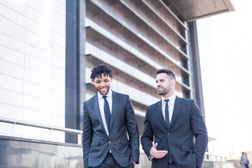 businessmen wearing suits walking and smiling and talking outdoor in a business area.