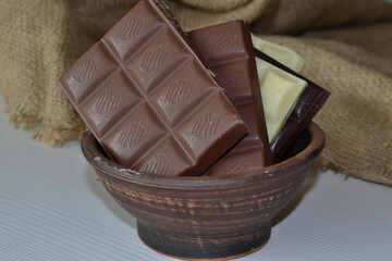 chocolate bars in a clay bowl on a white wooden table.