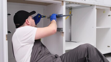The worker is assembling the design of kitchen furniture. Installation of new furniture.