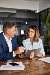 Mature 50s age Latin business man mentoring mid age European business woman discussing project on...