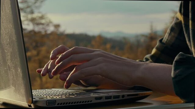 Traveler, traveler Works remotely sitting in the mountains looking into a laptop Outdoors. Smooth camera movement working woman mastering new techniques of testing herself in the wild, travel training