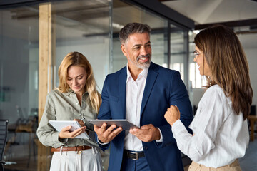 Group of diverse partners mature Latin business man and European business women discussing project on tablet in office. Team of colleagues professionals business people working together at workspace.