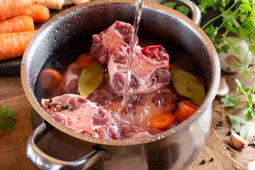 Raw veal beef Oxtail Meat with carrots, onions and spices in a saucepan on the table. Bone Broth Bouillon preparation