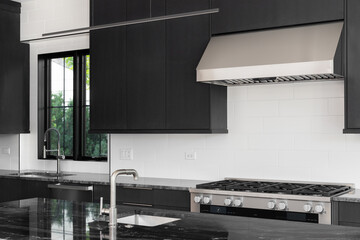 A modern kitchen detail with dark cabinet, white tile backsplash, stainless steel appliances, and a black marble countertop.