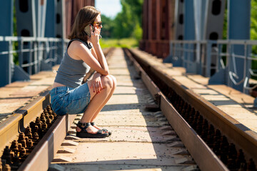 The girl sits on the rails and speaks on the phone