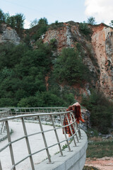 Red-haired confident full-length girl in an ethnic dress on a career background. Huge stones. Red hair develops in the wind. Concept. A symbol of will and indomitability