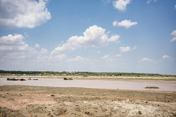 Shallow riverbed with scattered clouds and livestock in the water in hot summer day, Punjab, pakistan
