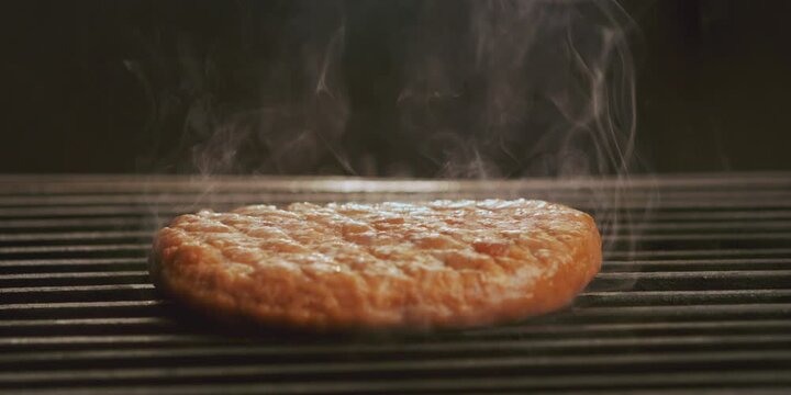 Slow-motion shot of a piece of hamburger patty burning on gas grill with smoke