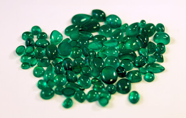 Pile of loose green emerald gemstones on a clean white background.