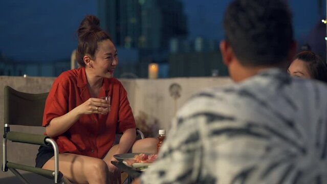 Group of Diversity Asian people friends enjoy and fun celebration meeting dinner party eating barbecue grill and drinking Korean vodka together at outdoor rooftop on summer holiday vacation at night.