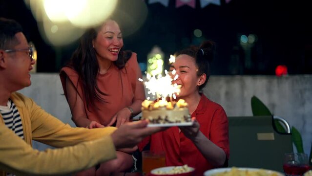 4K Diversity Asian people friends having celebration birthday party together at outdoor rooftop with food and drink. Adult Woman excited with birthday cake and blowing birthday candle with happiness.