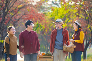 Obraz premium Happy Asian farmer family with senior parent are carrying produce harvest with homegrown organics apple, squash and pumpkin with fall color from maple tree during autumn season for agriculture usage