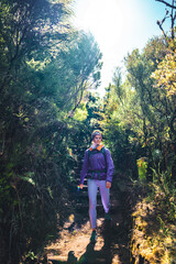 Female tourist with backpack hiking down stairs on footpath through a green forest on a sunny day. 25 Fontes Waterfalls, Madeira Island, Portugal, Europe.