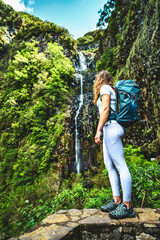 Naklejka na ściany i meble Athletic tourist with backpack standing on stone wall viewpoint and watches green overgrown Risco waterfall. 25 Fontes Waterfalls, Madeira Island, Portugal, Europe.